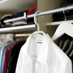 Chemises colorées et une chemise blanche en polyester, suspendues dans une penderie.