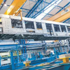 Szkielet wagonu kolejowego w hali produkcyjnej Alstom Chorzów, unoszony przez suwnicę.