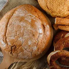 Różne rodzaje pieczywa: bochenek, paluszki sezamowe, obwarzanki i chleb z ziarnami.