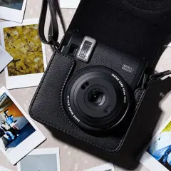 Czarny aparat Instax w futerale, otoczony natychmiastowymi zdjęciami. Dowiedz się, jak robić zdjęcia Instax, tworząc własne wspomnienia.