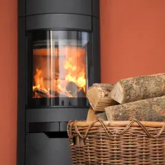 Moderner Kaminofen mit brennendem Holz. Ein Korb mit Holzscheiten daneben. Erneuerbare Energien, 15 Prozent Holz als Brennstoff.
