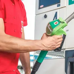 Un uomo in camicia rossa tiene una pompa di benzina verde con la scritta "Super 95".