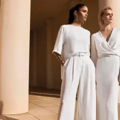 Due donne eleganti in bianco, un'ispirazione su come vestirsi ad un matrimonio con pantaloni a palazzo o abito lungo.