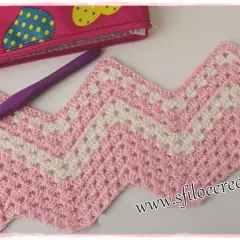 Uncinetto a zig zag rosa e bianco, con un uncinetto viola e una pochette a pois sullo sfondo.