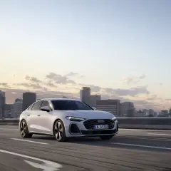Białe audi hybryda jedzie po autostradzie z widokiem na miasto o zachodzie słońca.