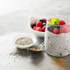 Pudding chia z malinami i borówkami, ozdobiony miętą, obok miseczki z nasionami chia.