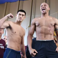 Two boxers face off. One, wearing a "team BIVOL" shirt, flexes his bicep. The other, with tattoos, shouts. Bivol fights in the light heavyweight class.