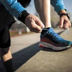 Un coureur attache ses lacets bleus, prêt à laisser une trace de frottement chaussure sur le bitume.