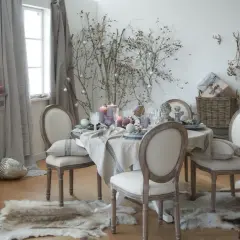 Stół nakryty do kolacji w stylu prowansalskim, ozdobiony gałązkami i świecami. Krzesła z tapicerką, dywany imitujące futro.