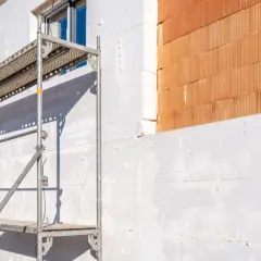 Budowa domu w toku: rusztowanie przy ścianie ocieplonej styropianem, obok cegła ceramiczna. Ile styropianu w paczce? Dużo!
