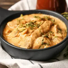 Cremiges Rindfleisch mit Pilzen, garniert mit frischem Thymian. Ein köstliches stroganoff rezept original, serviert in einer schwarzen Schüssel.