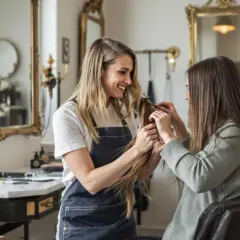 Coiffeuse souriante examine une mèche de cheveux, discutant du type de permanente avec sa cliente assise.