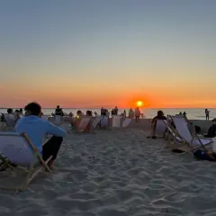 Zachód słońca międzyzdroje. Ludzie siedzą na leżakach na plaży, obserwując pomarańczowe niebo i morze.
