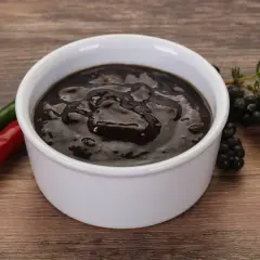 Gęsty, ciemny sos pieprzowy w białej miseczce, obok czerwona i zielona papryczka chili oraz gałązka jeżyn.