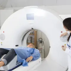 Pacjentka leży na stole tomografu komputerowego, a lekarka przygotowuje badanie. Dowiedz się, ile trwa tomografia komputerowa.