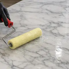 Mano guantata applica resina epossidica per marmo con un rullo, creando una finitura lucida e protettiva.
