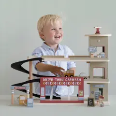 Uśmiechnięty chłopiec bawi się drewnianym garażem Little Dutch z myjnią i stacją benzynową.