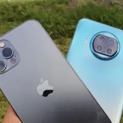 Porównanie aparatów: iPhone (iOS) kontra Xiaomi (Android). Dwa smartfony na tle zielonej trawy.
