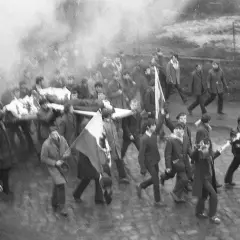 Tłum niesie nosze z ciałem, dym unosi się w powietrzu. Janek Wiśniewski padł, a jego towarzysze idą dalej.