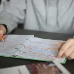 Ręka pisze ołówkiem w zeszycie, podkreślając ważne fragmenty. Czy to przygotowania do egzaminu, od jakiej średniej jest 6?