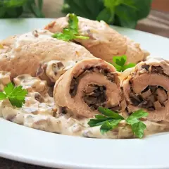 Roladki z indyka duszone w sosie grzybowym, podane na białym talerzu z natką pietruszki.