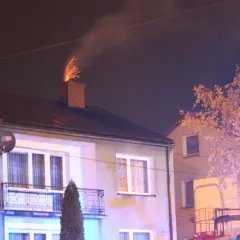 Jasny komin z cegły, z którego lecą iskry, sugeruje, dlaczego lecą iskry z komina. W tle widać dom i drzewo.