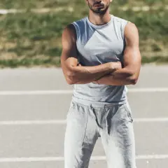Mężczyzna w szarym podkoszulku i dresie zielonym męskim stoi na bieżni.