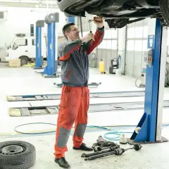 Mecánicos trabajando en el mantenimiento de coches en un taller. Uno usa una llave inglesa en el coche elevado, otro se prepara.