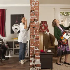 Mężczyzna siedzi przy stole, kobieta przygląda się zniszczonej ścianie, a starsza pani gra na gitarze. Zakłócanie miru domowego w najlepszym wydaniu.