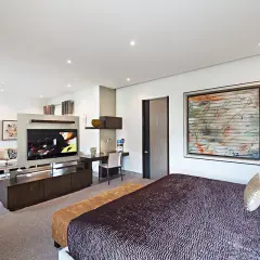 Modernes Schlafzimmer mit einem großen Fernseher im Wohnbereich, der durch eine Trennwand vom Bett abgetrennt ist.