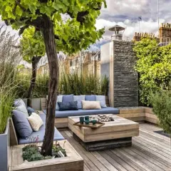 Aménagement autour d'une terrasse avec banquette bleue, table basse en bois et végétation luxuriante. Un espace détente chic et verdoyant.