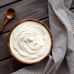 Prosty krem z mascarpone i jogurtu w drewnianej misce, obok drewniana łyżka i pasiasty ręcznik.