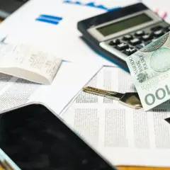 Dłoń trzyma banknot 100 zł obok klucza i dokumentów. Rozważasz grupy podatkowe darowizna?