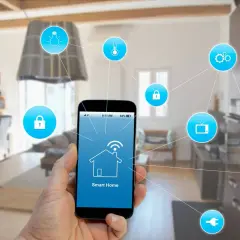 Mano sujetando smartphone con app "Smart Home" para control de instalación domótica. Iconos de seguridad, luz, temperatura, TV, nevera y enchufe conectados.