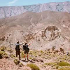 Deux randonneurs bras ouverts contemplent un paysage désertique spectaculaire lors d'une randonnée Atlas Maroc. D'autres marcheurs sont visibles au loin.