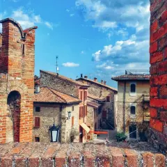 Un antico borgo vicino Parma, con case in pietra e tetti rossi, incorniciato da mura di mattoni sotto un cielo azzurro e nuvoloso.