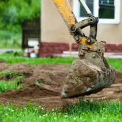 Koparka z brudną łyżką pracuje na nierównym terenie. Może to oznaczać kary za niwelację terenu.