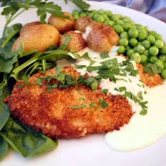 Krispig schnitzel med krämig sås till, serverad med småpotatis, gröna ärtor och färsk spenat.