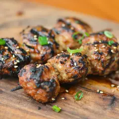 Skewered, grilled Japanese meatballs glazed with a savory sauce, sprinkled with sesame seeds and green onions.