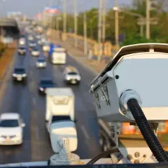 Kamera monitorująca ruch drogowy. Czy policja może wykryć antyradar? Zbliżenie na białą kamerę z kablem, w tle ruchliwa autostrada.