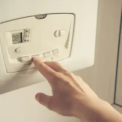 Main d'une personne appuyant sur les boutons d'une pompe à chaleur. Faut-il éteindre sa pompe à chaleur l'été ?