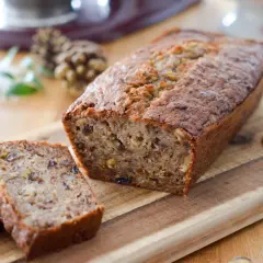 Un délicieux cake banane, coupé en tranches, sur une planche en bois. Des noix et des biscuits complètent cette gourmandise.