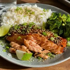 En läcker tallrik med asiatisk lax i ugn, serverad med ris, broccoli och limeklyftor.