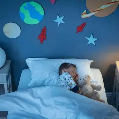 Kleiner Junge schläft im Weltraum-Kinderzimmer. Die kinderzimmer wandgestaltung mit Planeten und Raketen inspiriert Träume von Abenteuern.