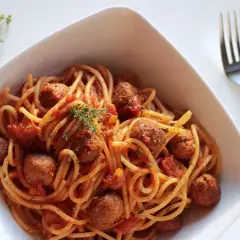 Pyszne spaghetti z klopsikami w sosie pomidorowym, udekorowane gałązką tymianku. Idealne pytanie: jakie przyprawy do spaghetti?