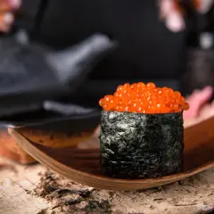 Wykwintny gunkan sushi z łososiem ikra, owinięty w ciemne nori, prezentowany na drewnianej łódce.
