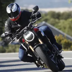 Motociclista con casco Venom en pleno rodaje moto, inclinado en una curva con paisaje verde de fondo.
