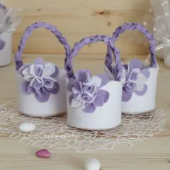 Piccoli cestini porta bomboniere fai da te in feltro bianco con fiori lilla e manici intrecciati, perfetti per un evento speciale.