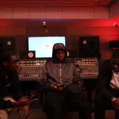 Trois jeunes hommes dans un studio d'enregistrement, discutant peut-être d'un cover rap gratuit.