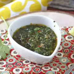 Un tazón blanco con una deliciosa **receta de chimichurri** casera, adornado con cilantro fresco y una rodaja de limón.